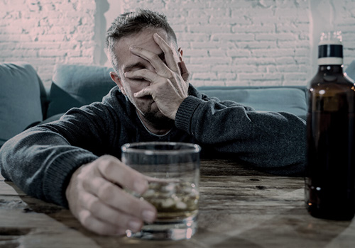 Мужчина сидит за столом с бутылкой и бокалом